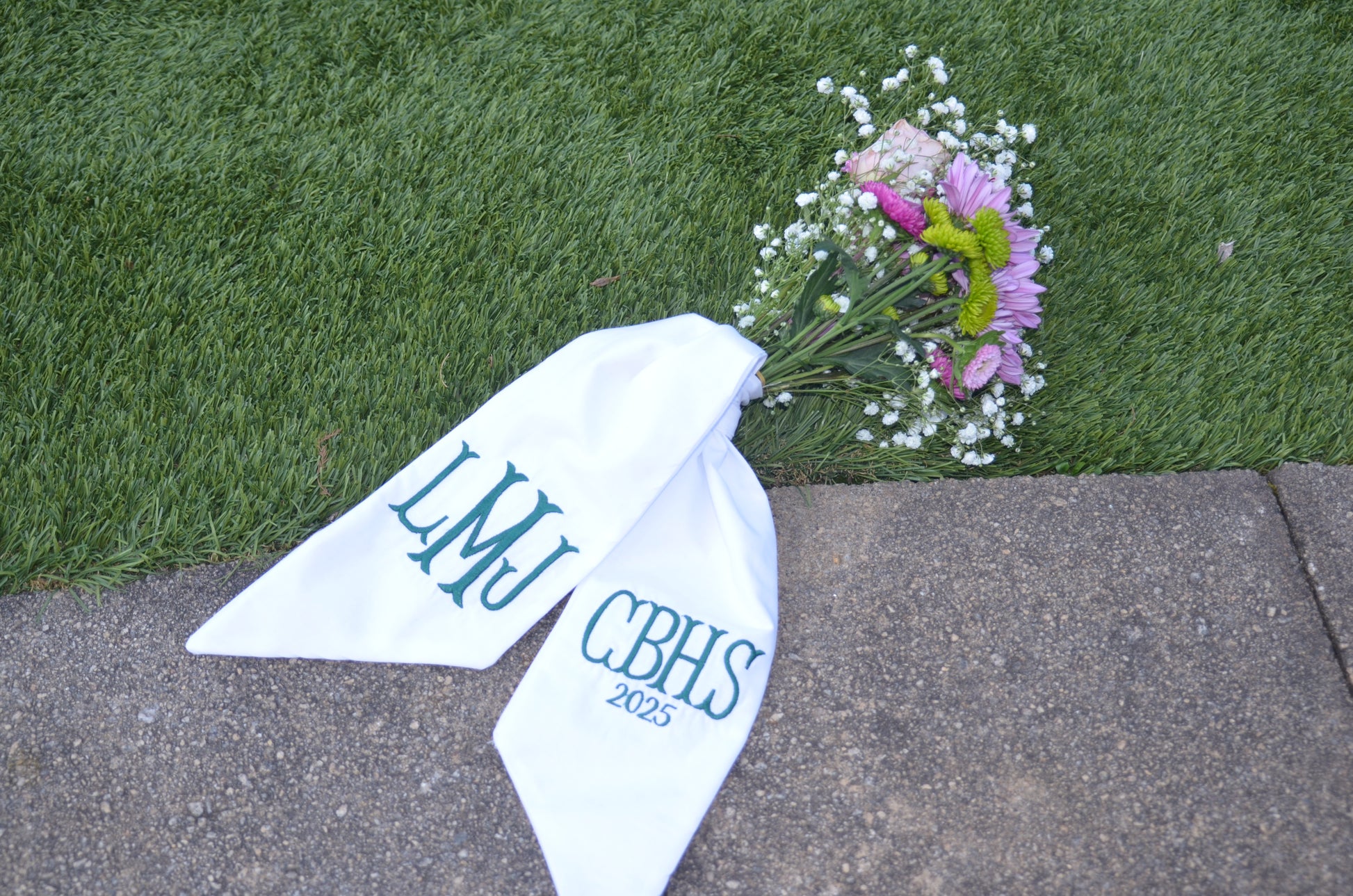 White bandana with 'LMU CBHS 2023' text on grass and pavement