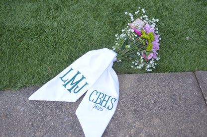 White bandana with 'LMU CBHS 2023' text on grass and pavement