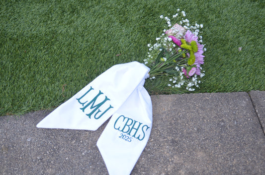 White bandana with 'LMU CBHS 2023' text on grass and pavement